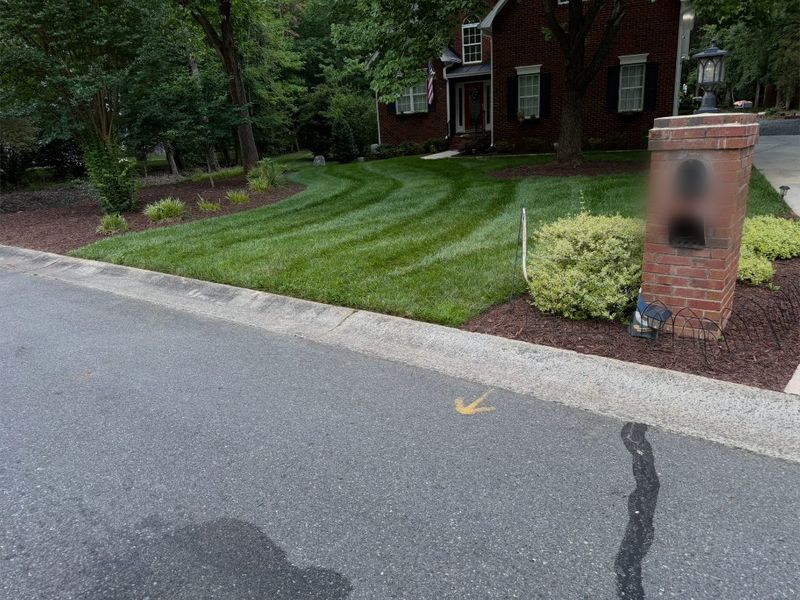 Striped front lawn sweeping up to a two-storey brick house